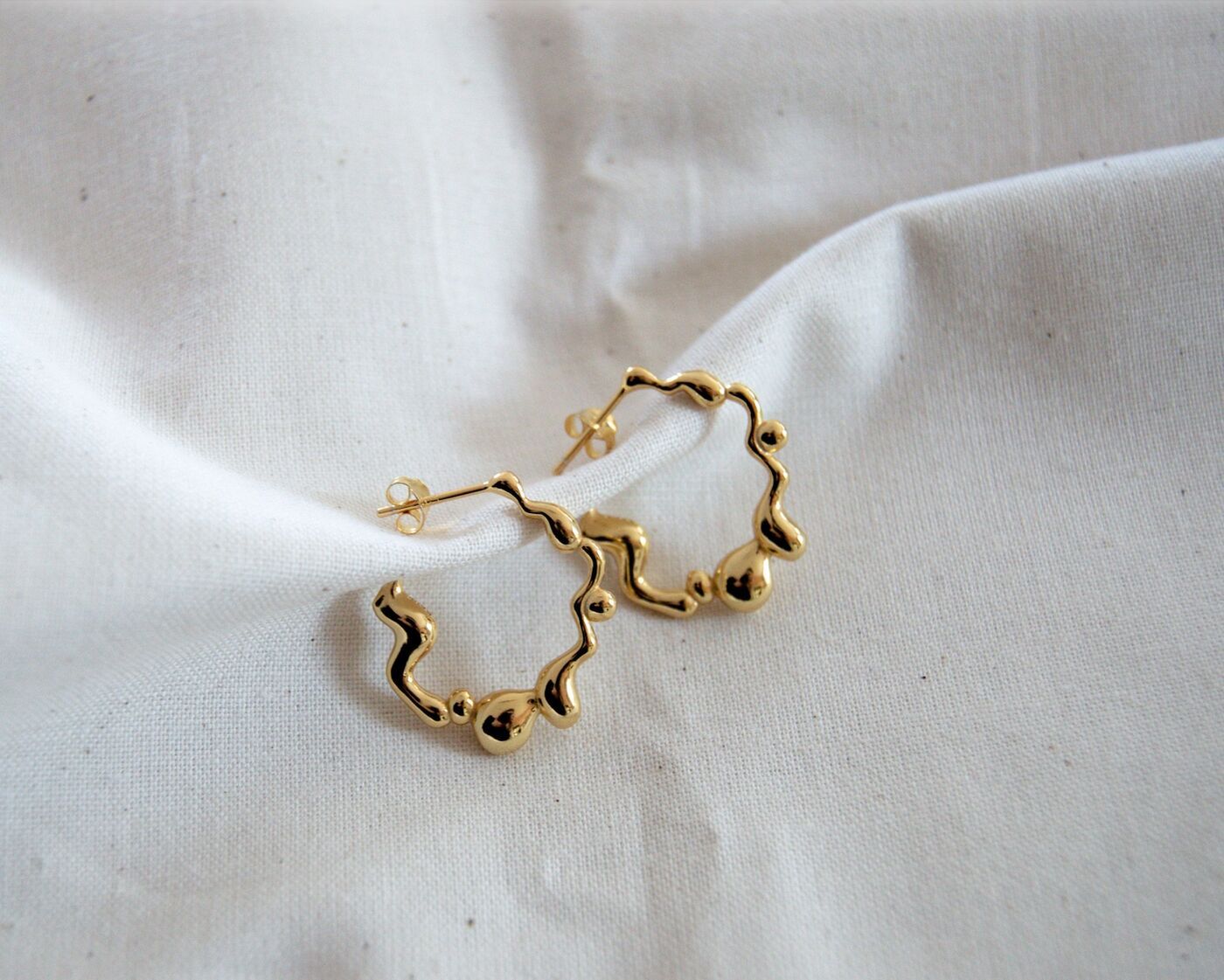 Sculptural gold hoop earrings on white linen